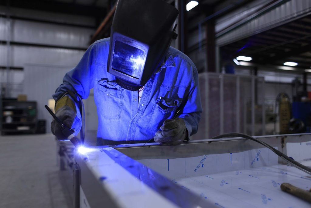 Photo of a man wearing welding mask and welding an aluminium panel.